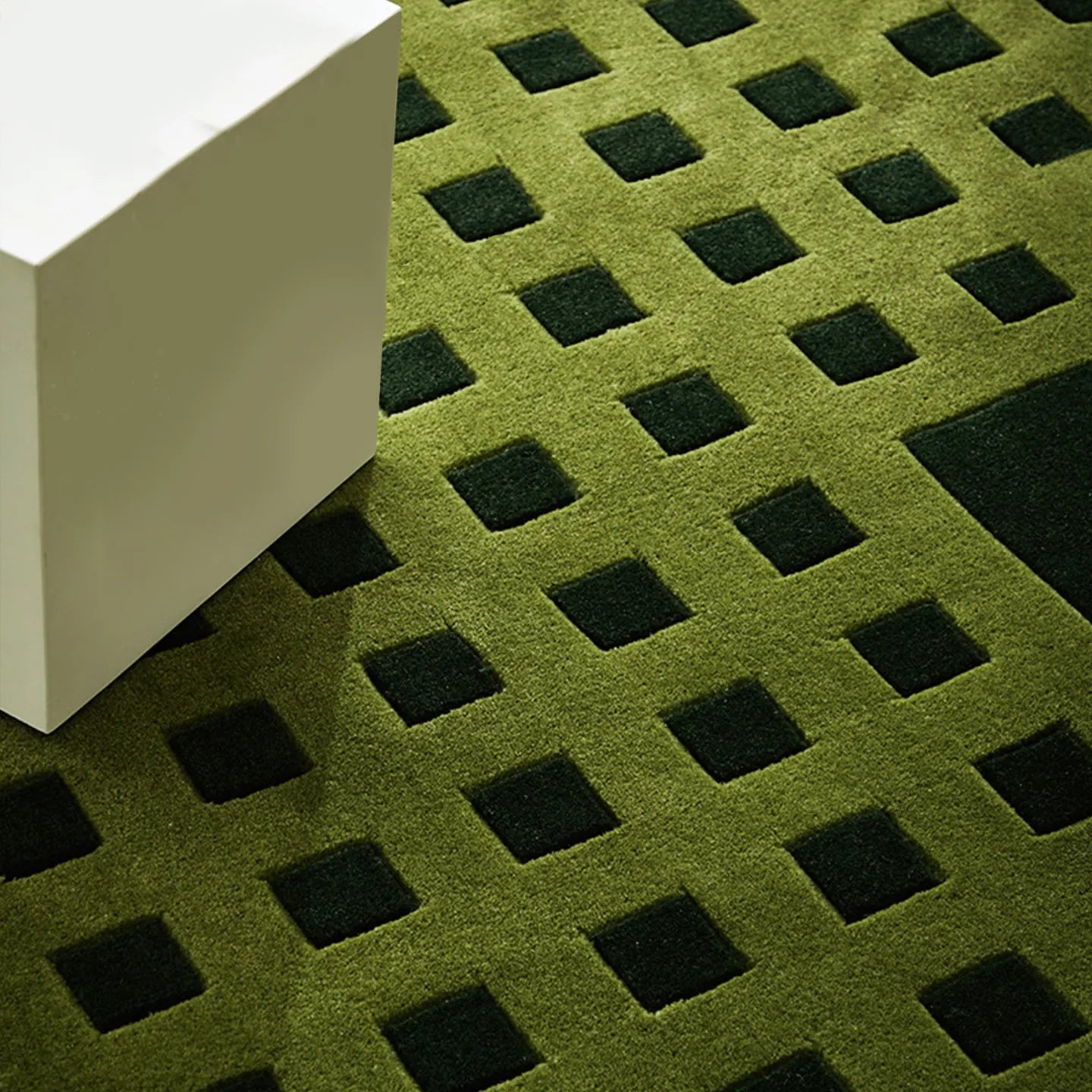 Close-up of Tessera Olive Green Grid Modern High Low Rug by Housenfriends with a white block, showing texture and detail.