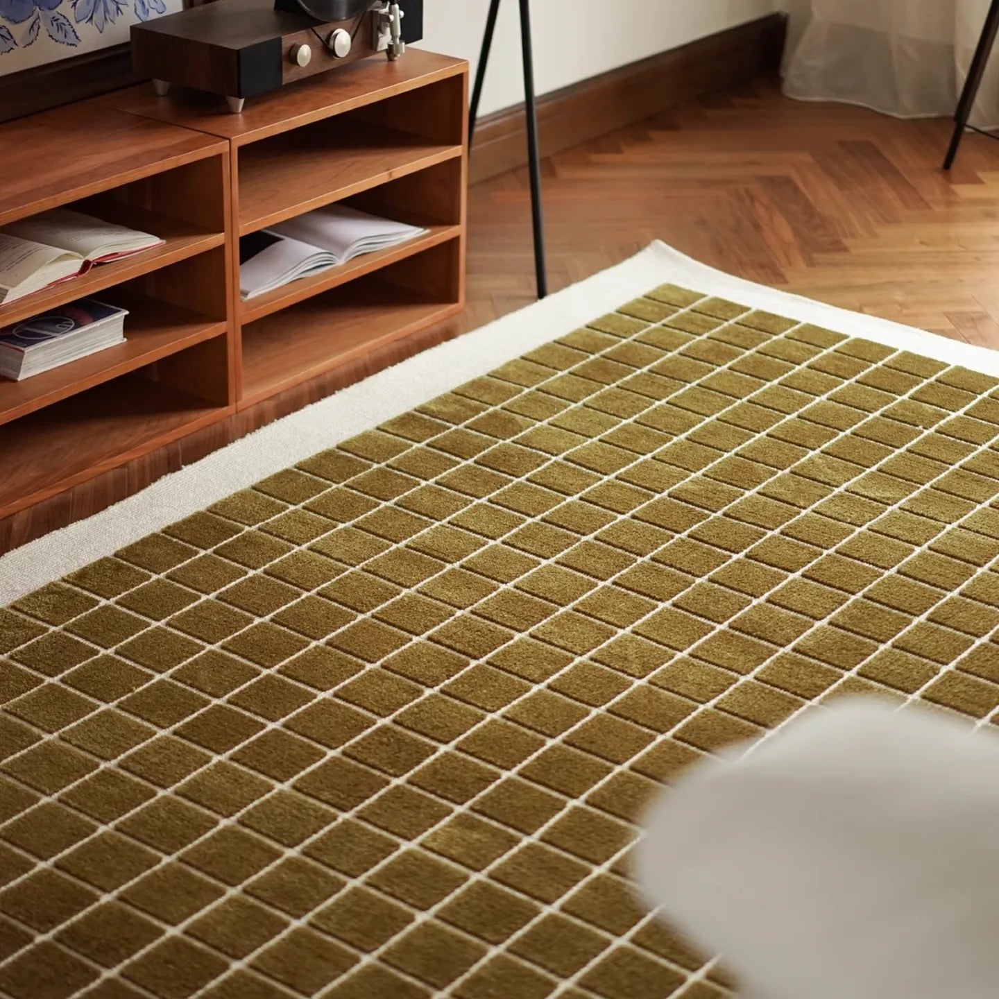 Olive green grid-patterned rug on a wooden floor with a shelf in the background
