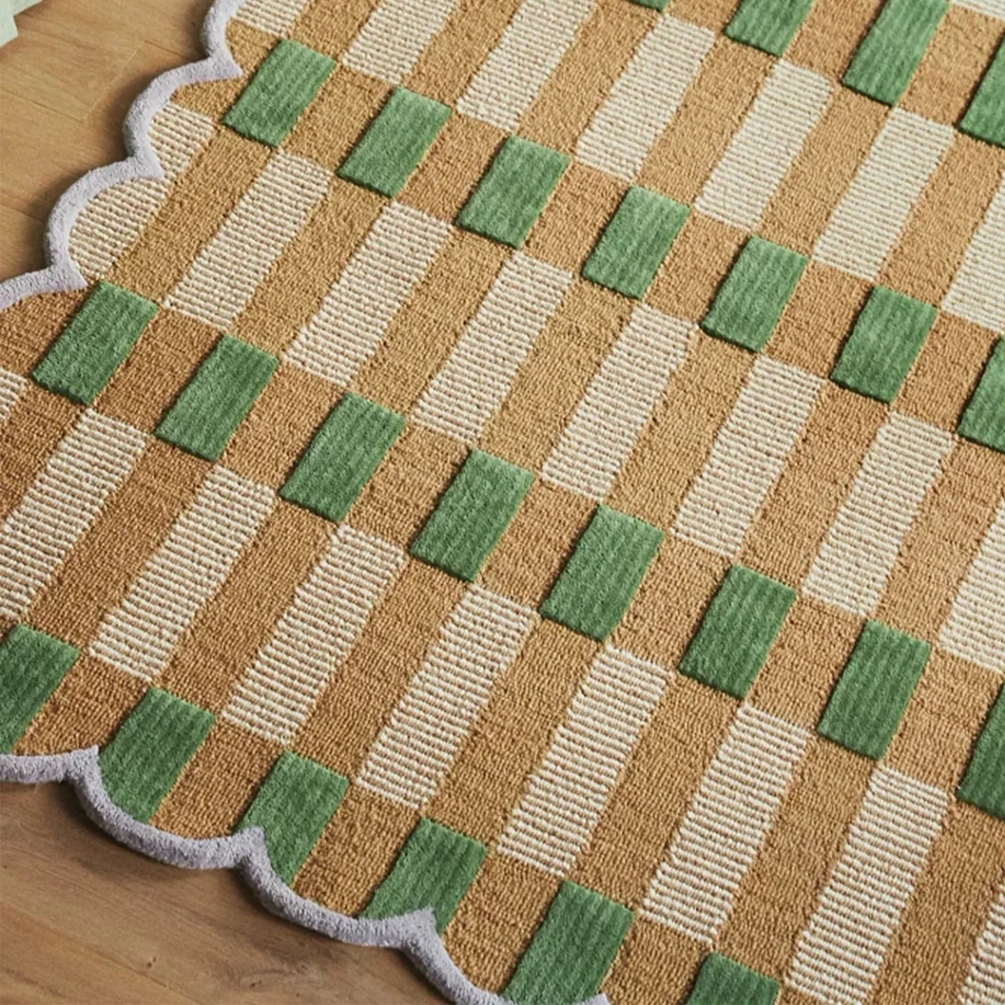 Close-up of pastel green and orange gingham wavy rug by Housenfriends on a wooden floor
