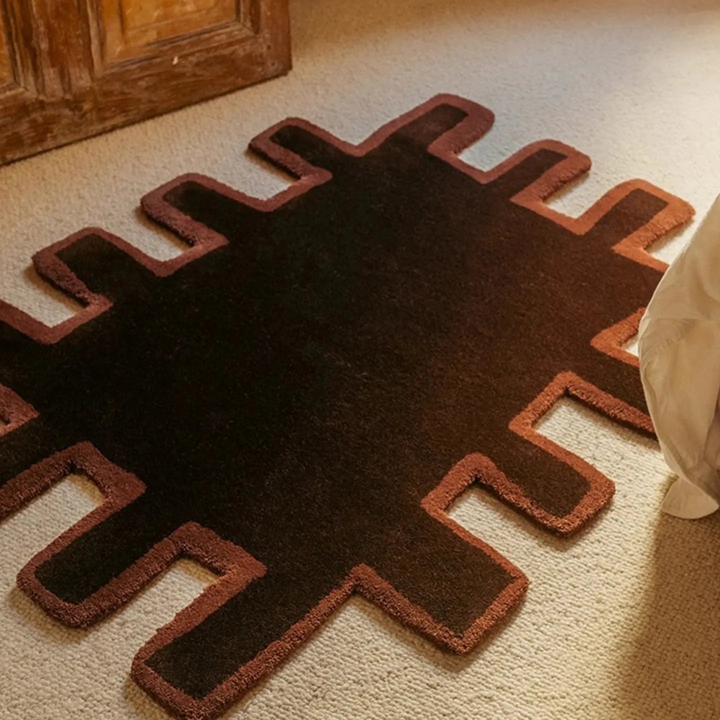 Biscuit shaggy abstract geometric rug by Housenfriends in chocolate brown with a brown border, on a beige carpeted floor.