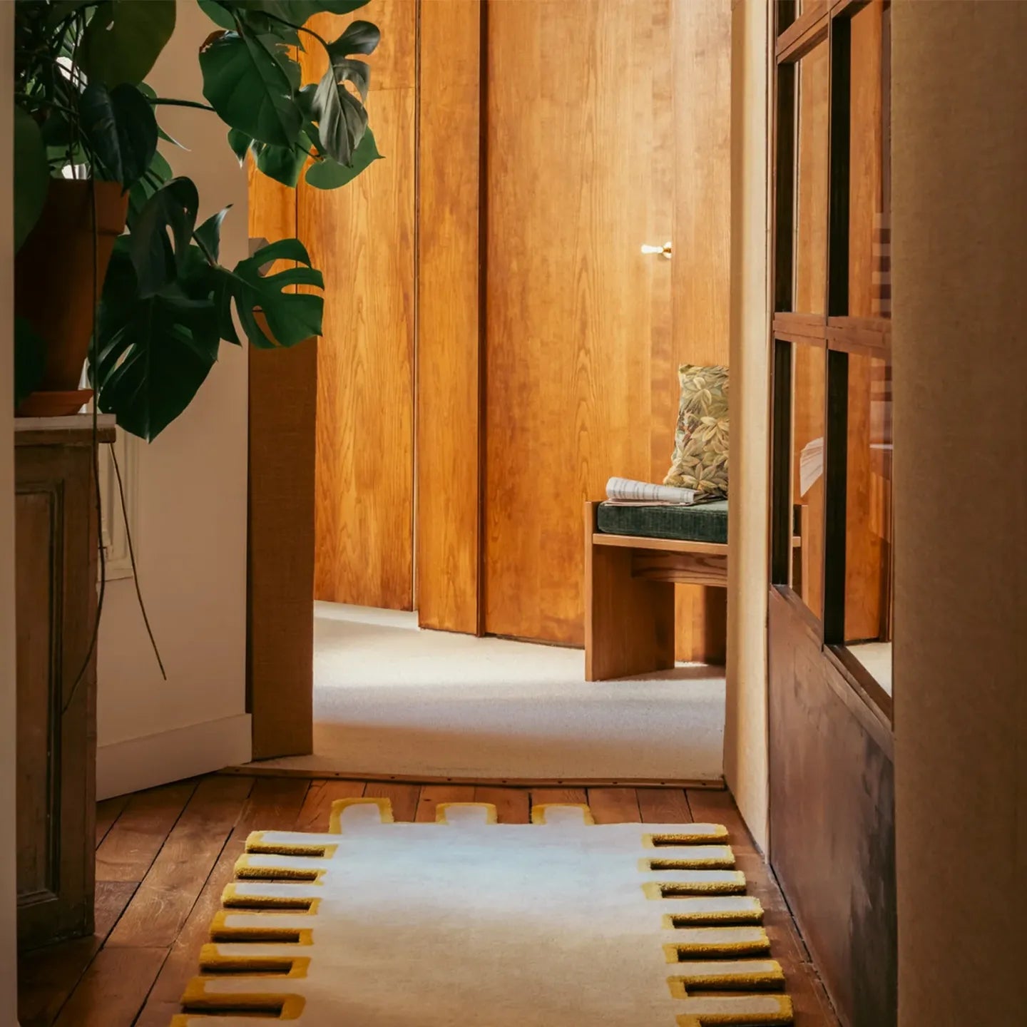 Biscuit beige shaggy abstract geometric rug by Housenfriends in a hallway with wooden walls, a bench, and green plants.