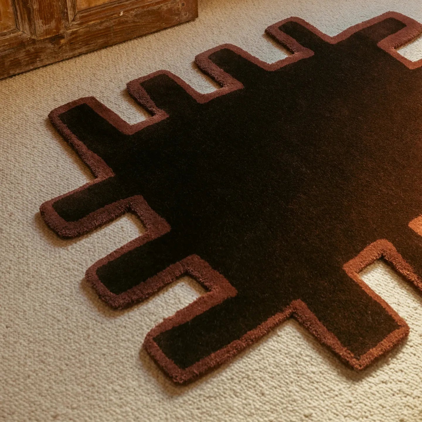 Biscuit shaggy abstract geometric rug by Housenfriends in chocolate brown with a brown border, on a beige carpeted floor.