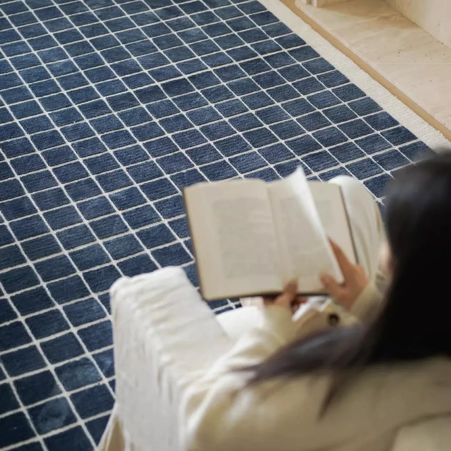 Person sitting on the Salina navy blue checkered modern rug by Housenfriends, reading a book.