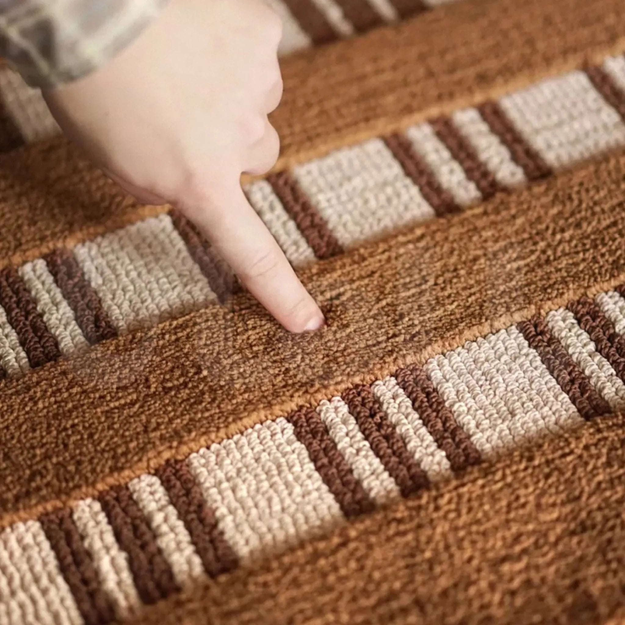 Close-up of a hand pointing at a striped patterned rug with brown and beige colors.