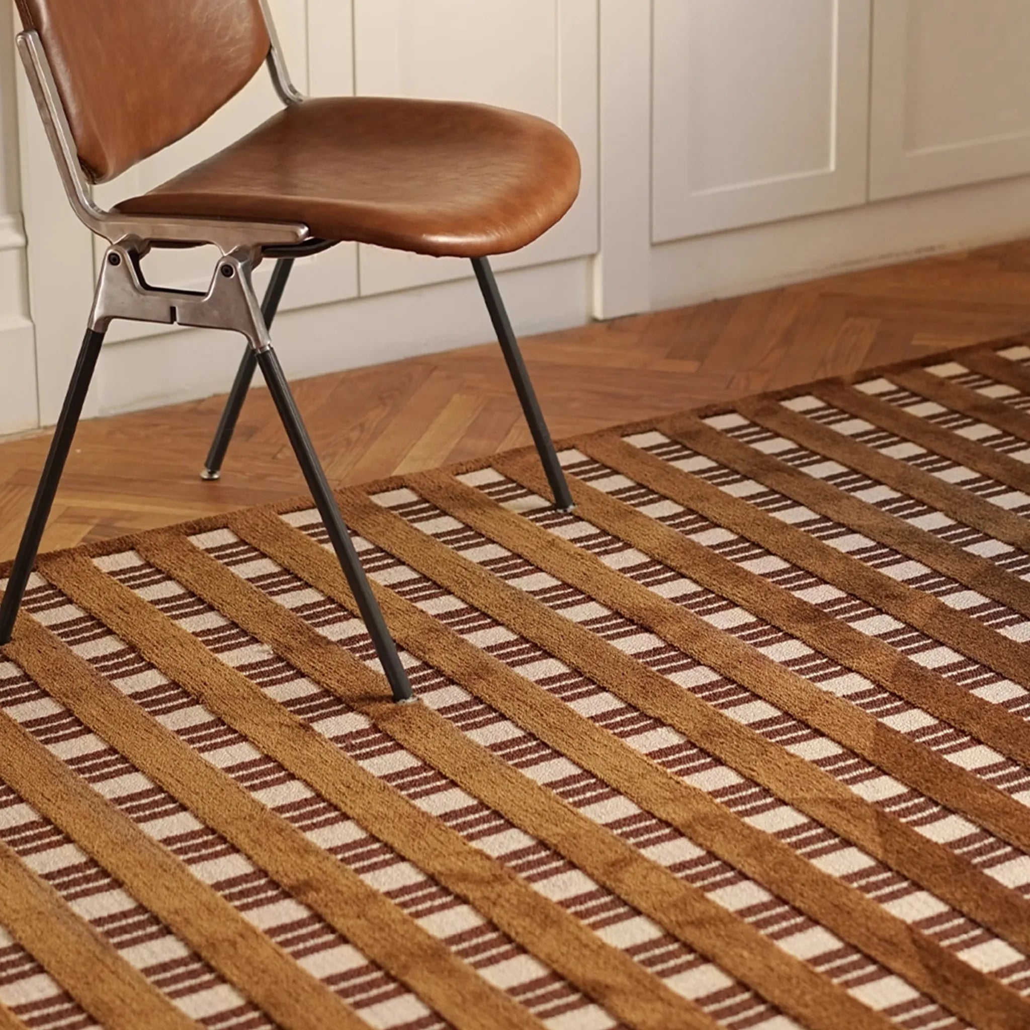 Brown chair on Amber Brown and Cream Checkered Textured Rug in a room with wooden flooring.