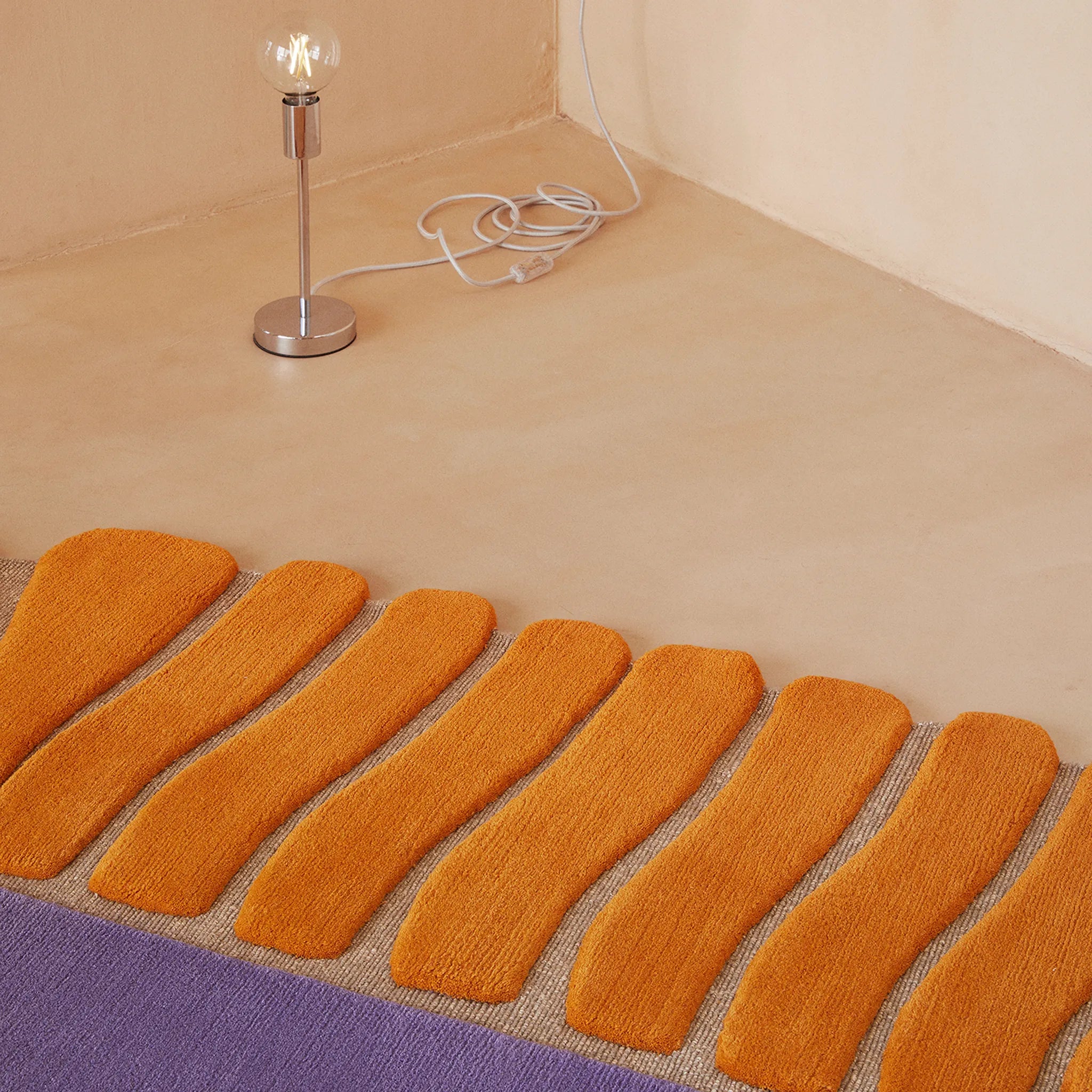 Coquille Purple Orange Seashell Shaped Sculpted Rug by Housenfriends on a beige floor with a small lamp.