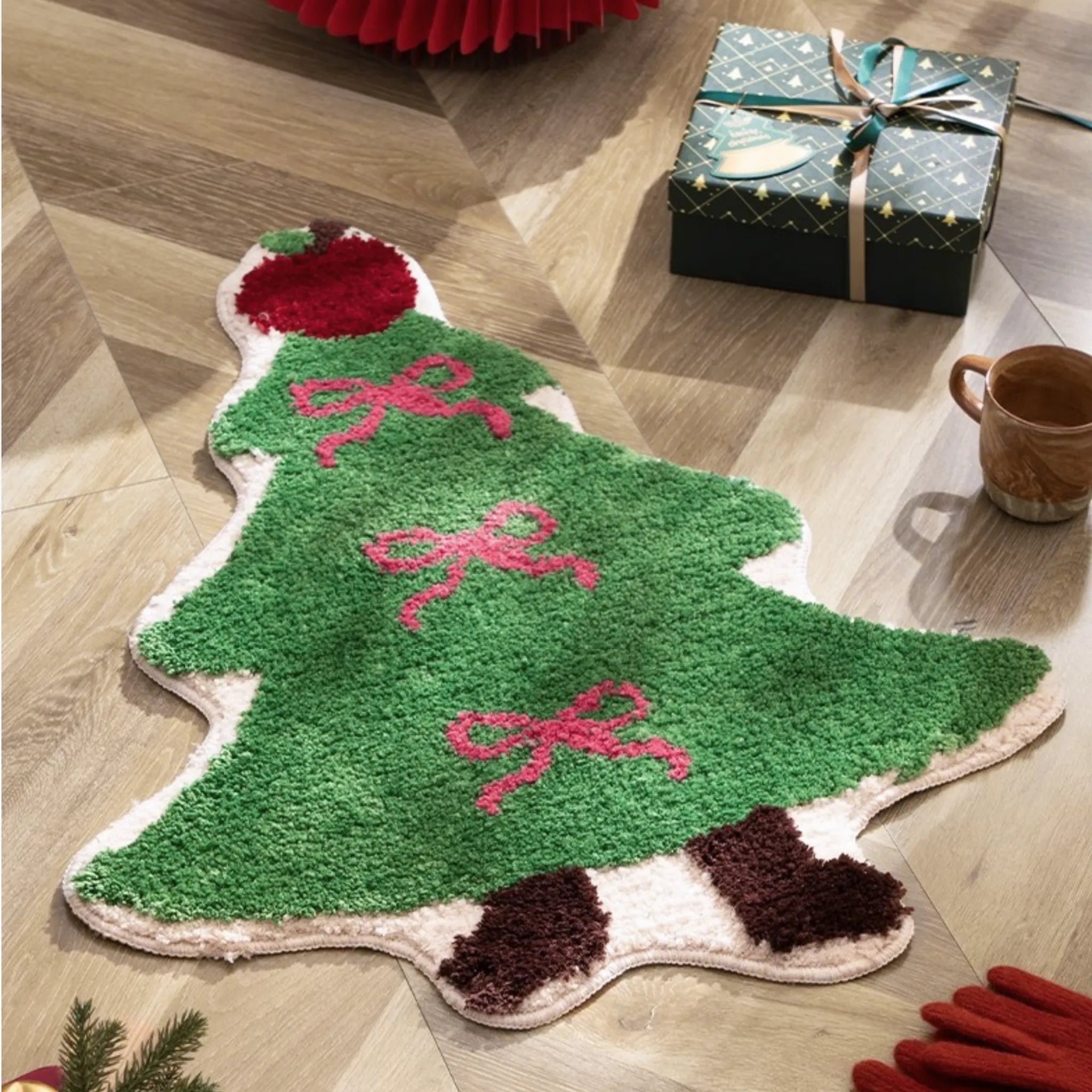 Green Christmas tree-shaped tufted rug by Housenfriends on a wooden floor with wrapped gifts.