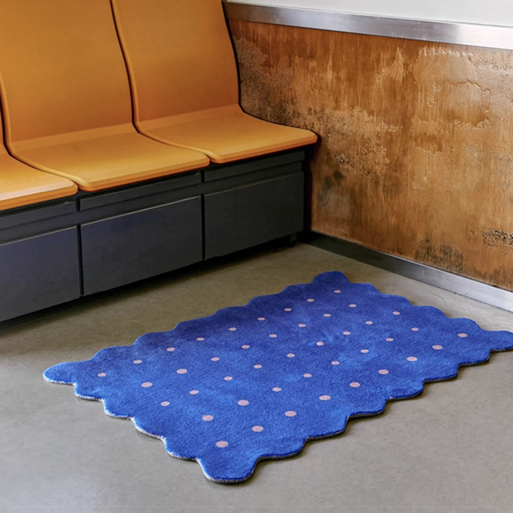 Arden Klein Blue & Pink Polka Dots Scalloped Rug by Housenfriends on a gray floor in front of orange benches.