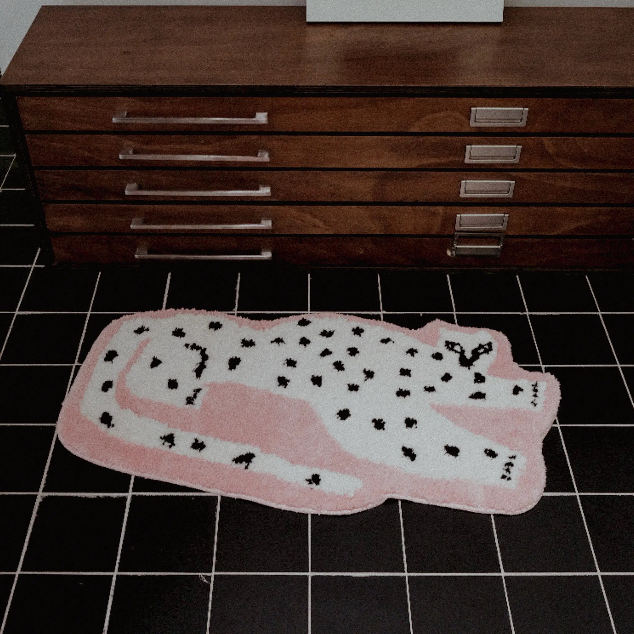 Blossom Pink Base White Leopard Shaped Tufted Rug on a black tiled floor with wooden furniture