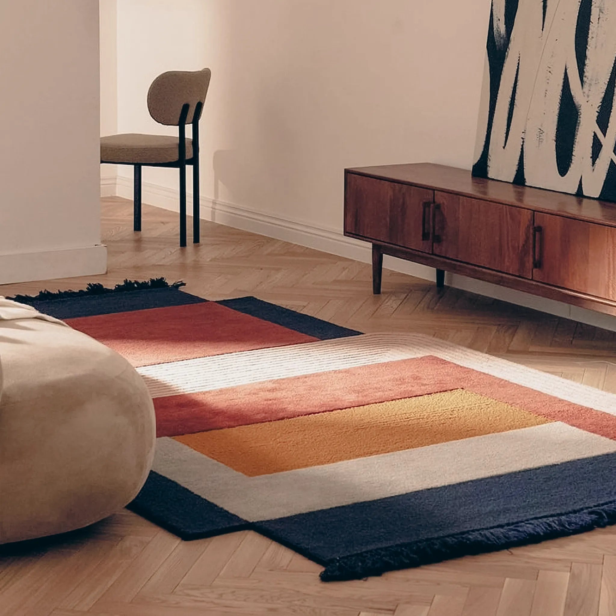 Mira Rust Mustard Navy Pink Grey Abstract Irregular Fringe Wool Rug on a wooden floor with a wooden cabinet and chair.