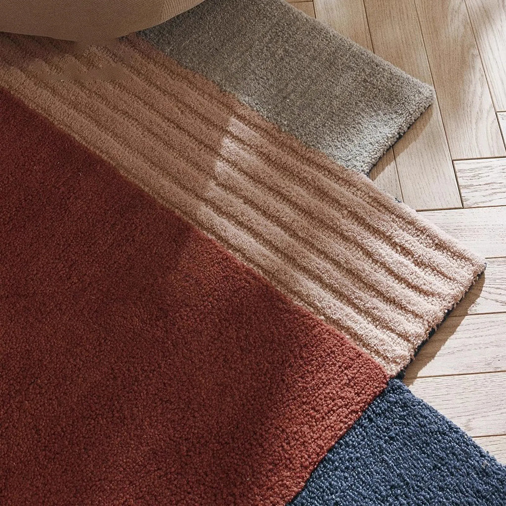 Close-up of rug texture in red, pink, grey, and blue on a wooden floor.