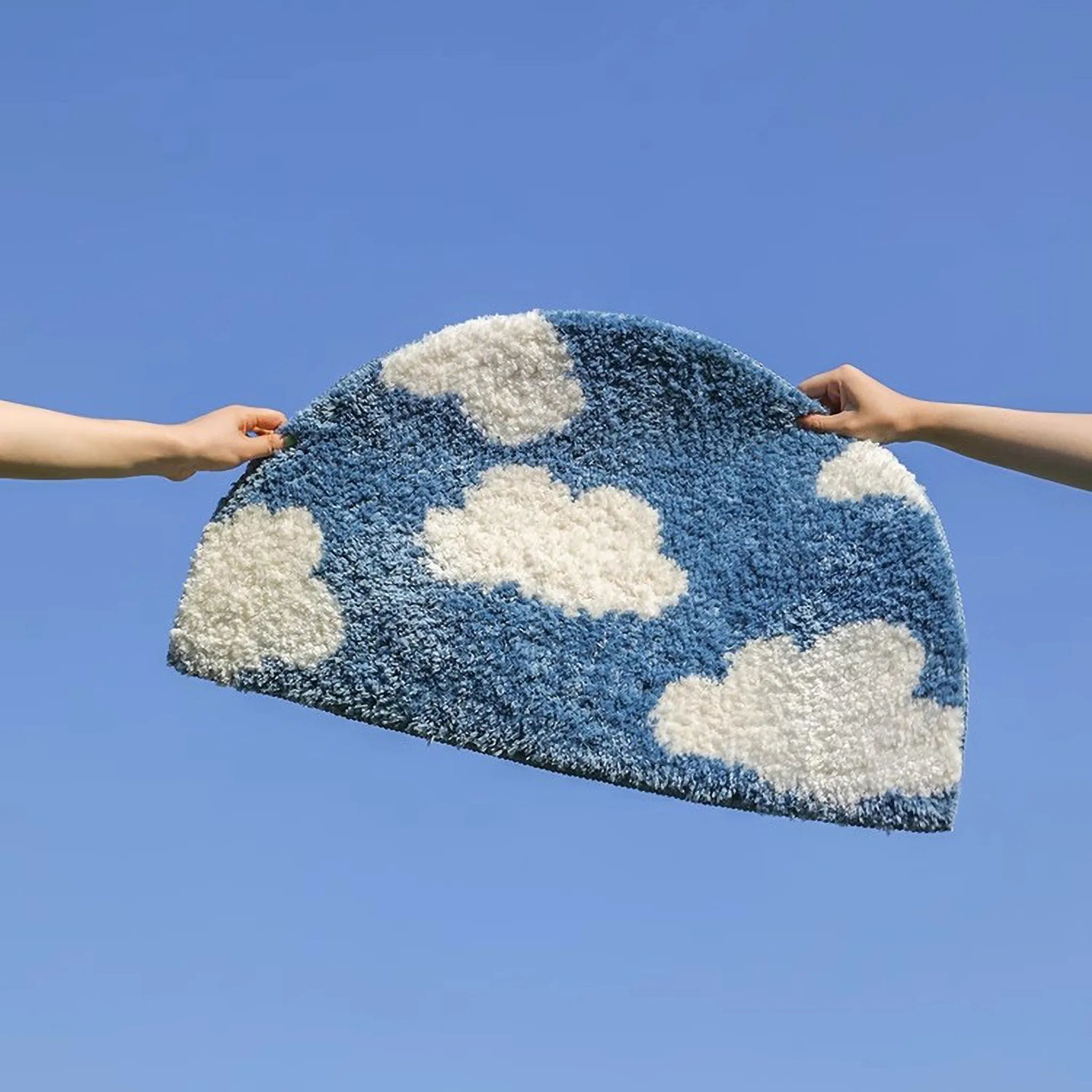 Seren Blue & White Half-Moon Cloud Tufted Rug by Housenfriends held by two hands against a clear blue sky.