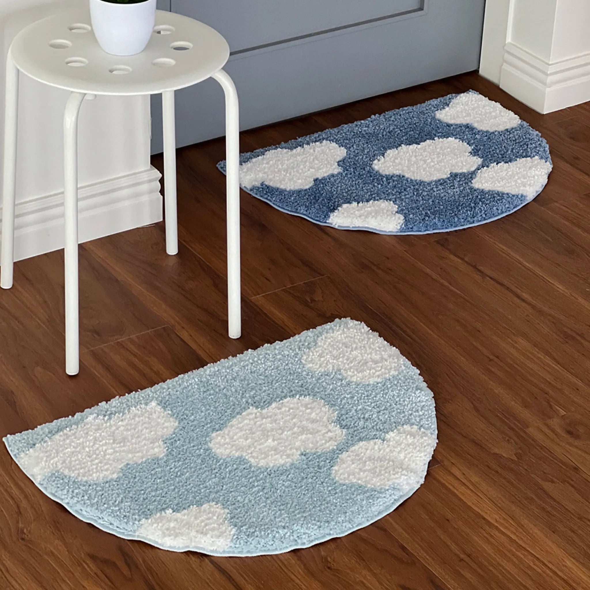 Two cloud-patterned tufted rugs by Housenfriends on a wooden floor with a white stool.
