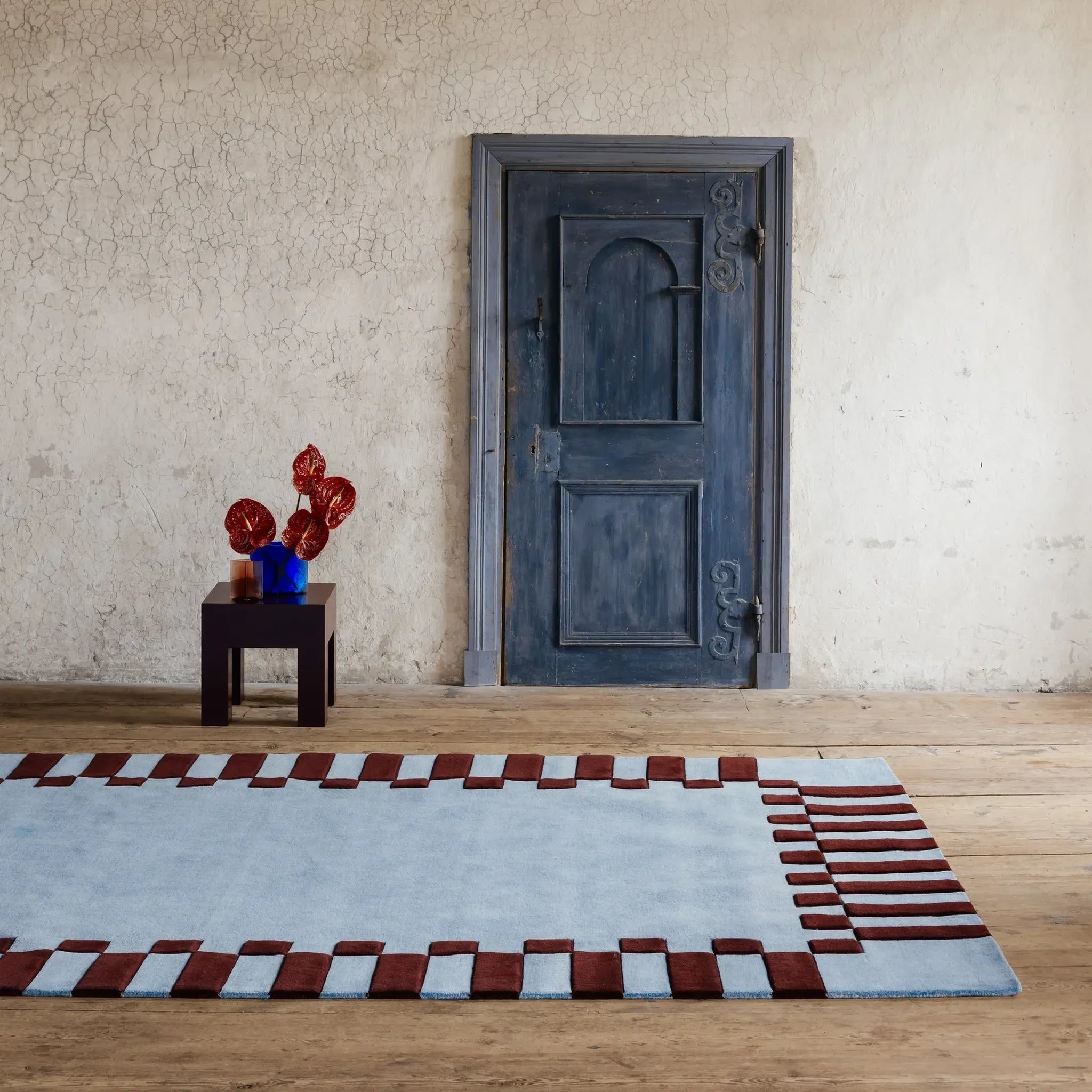 Room with a blue door, table with flowers, and Acropolis Slate Blue and Red High Low Wool Rug by Housenfriends