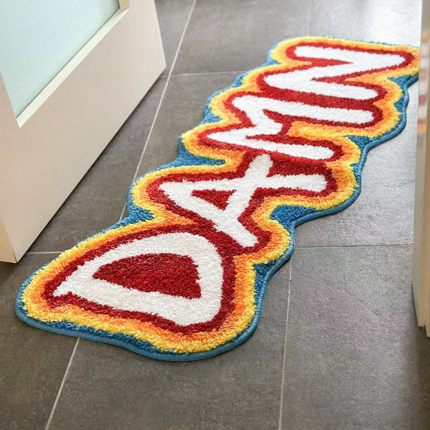 A hand-tufted rainbow coloured runner rug by Housenfriends with the word 'DAMN', on the bathroom’s tiled floor