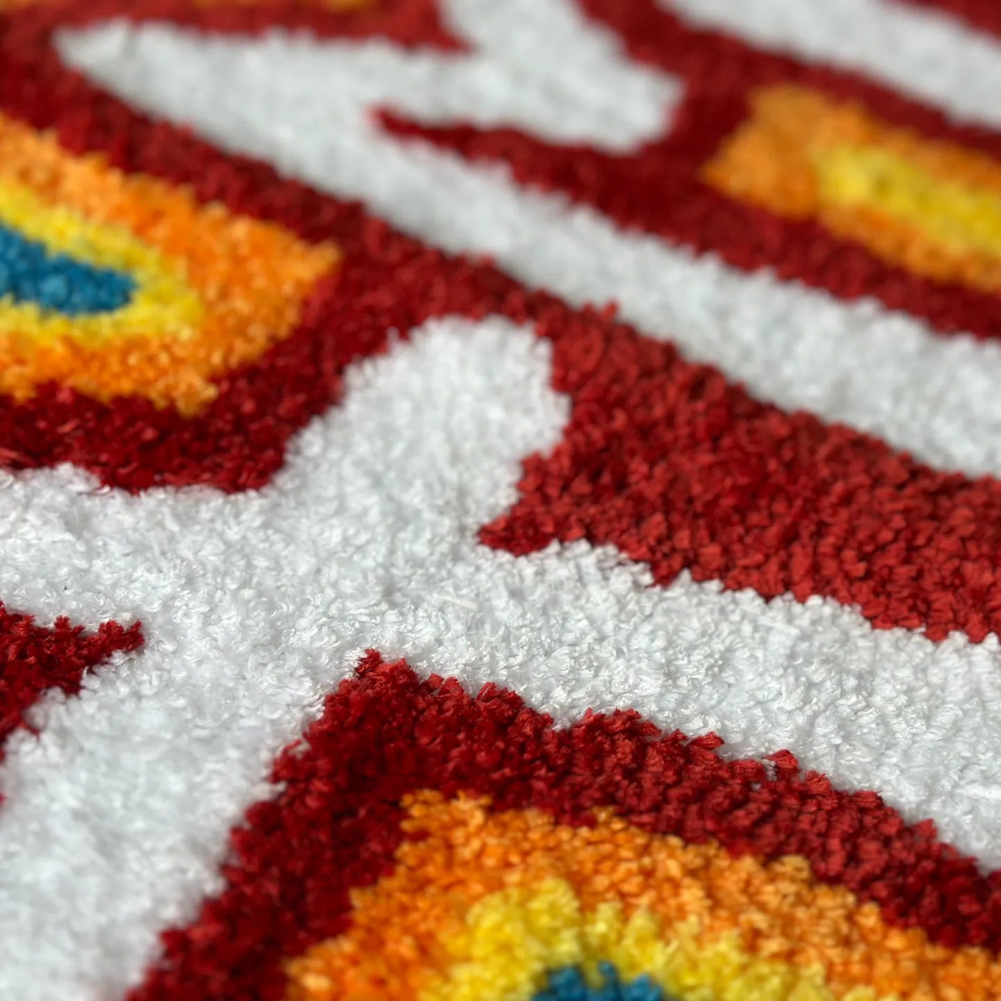 Close-up of a hand-tufted rainbow coloured runner rug by Housenfriends with the word 'DAMN' in red, orange, and white.