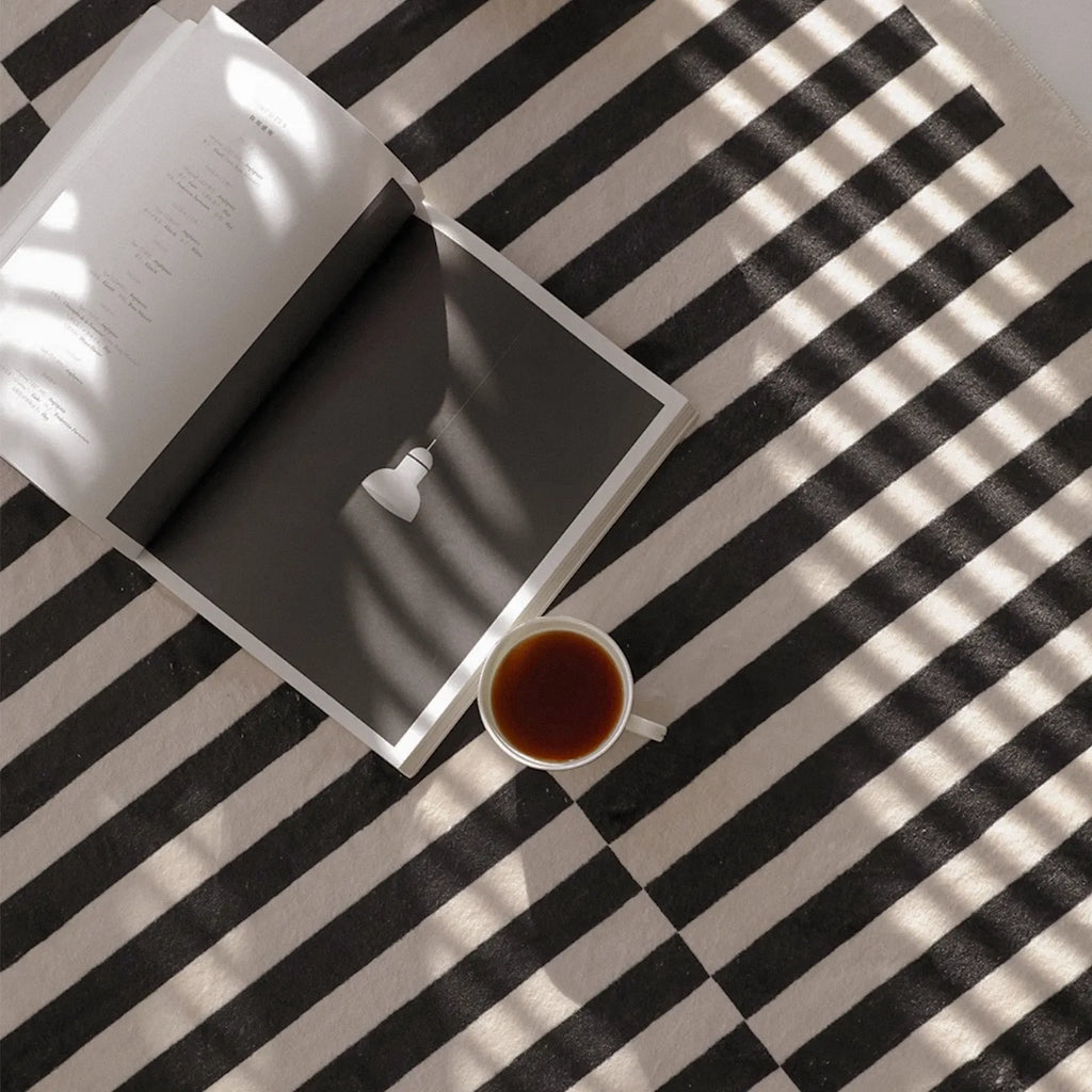 Open book and cup of tea on Stockholm Black and White Modern Offset Stripe Rug by Housenfriends