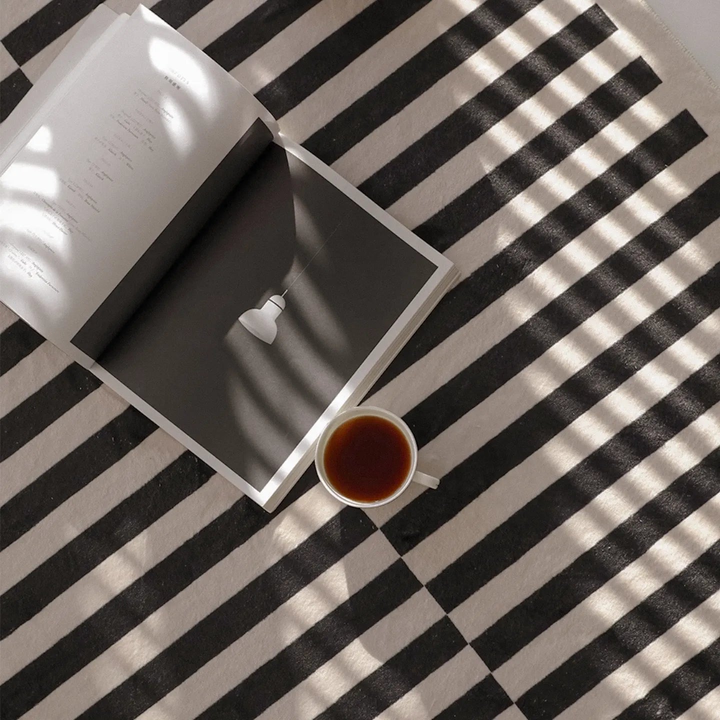 Open book and cup of tea on Stockholm Black and White Modern Offset Stripe Rug by Housenfriends