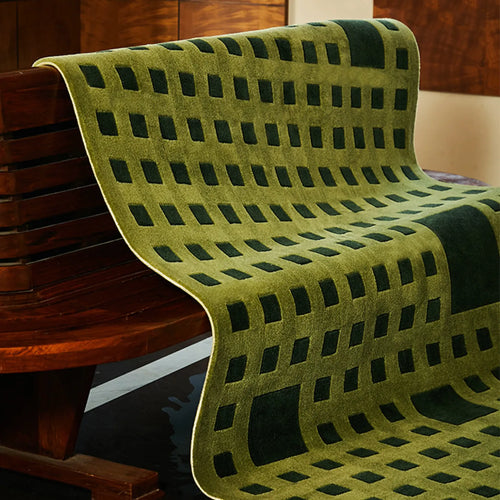 Tessera Olive Green Grid Modern High Low Rug by Housenfriends, draped over a wooden bench for a layered look.