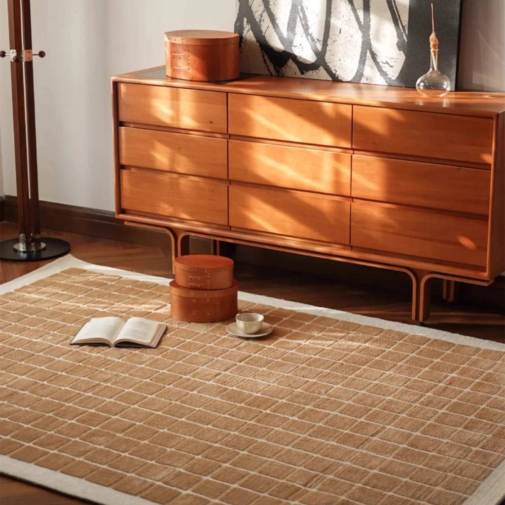 Wooden dresser with decorative items on a white rug featuring a caramel gold grid pattern by Housenfriends