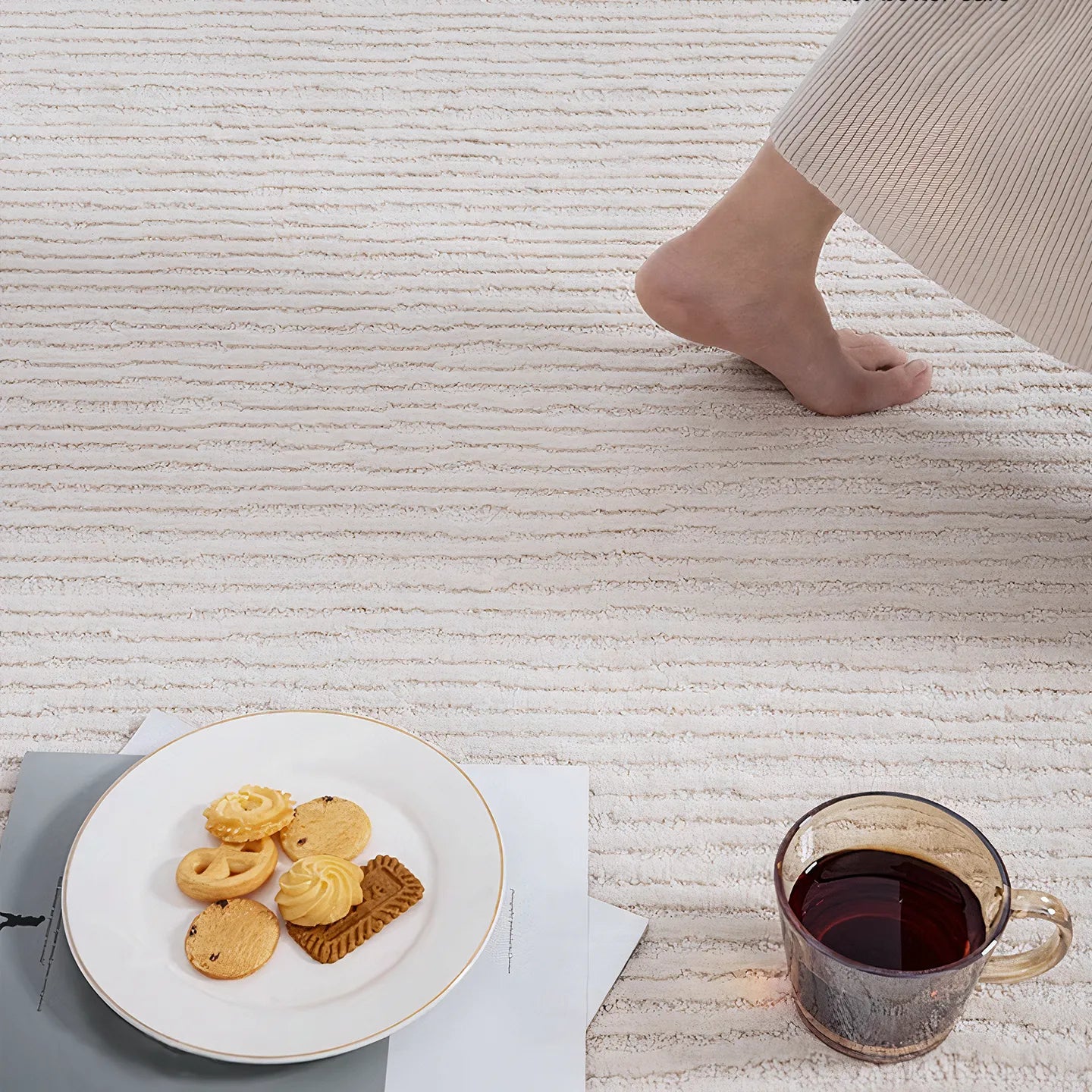 Cosy afternoon with tea and cookies on Rae off-white modern rug by Housenfriends, foot in background.