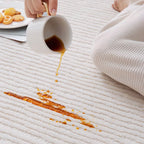 Close-up of coffee spilling on Rae off-white modern rug by Housenfriends, with water-resistant, easy-to-clean surface.
