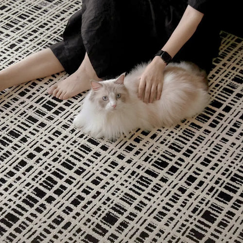 Person petting a fluffy white cat on a Jules Black White Modern Grid Pattern Rug by Housenfriends