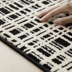 Close-up of Jules Black White Modern Grid Pattern Rug by Housenfriends with a hand touching the fabric