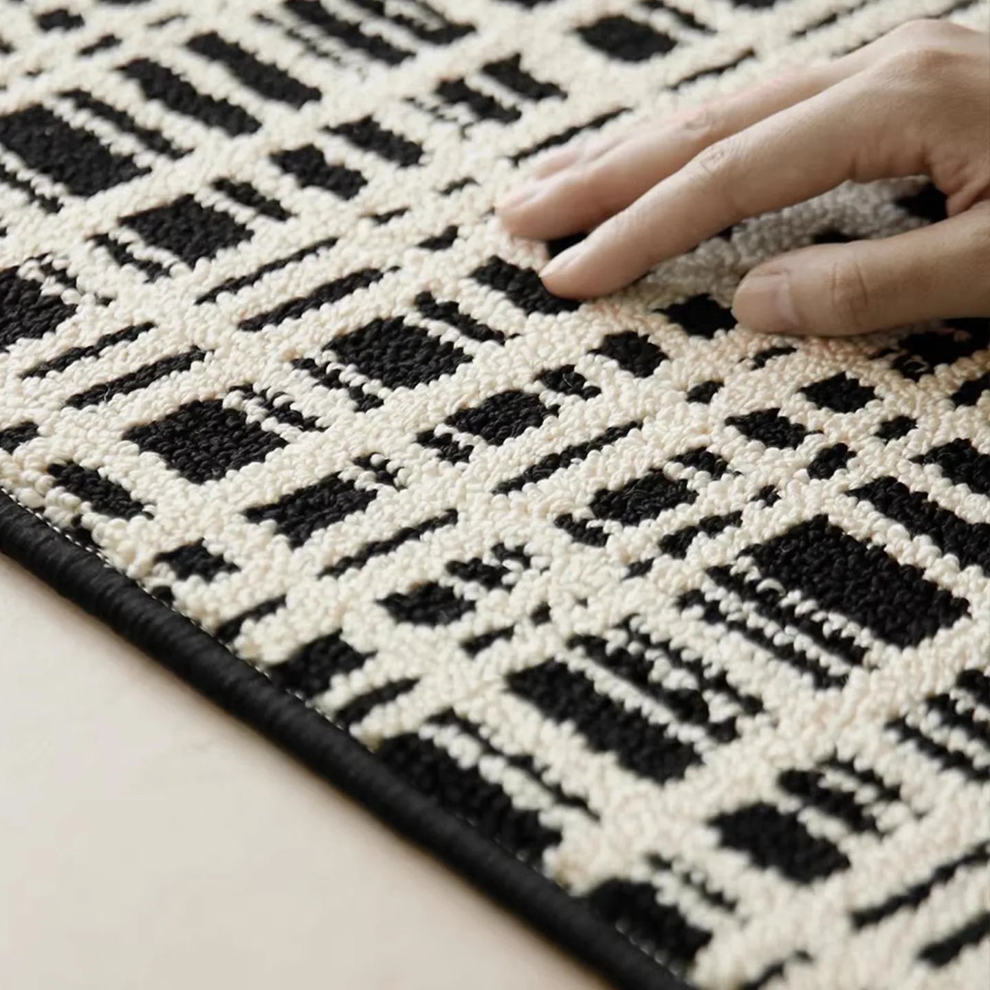 Close-up of Jules Black White Modern Grid Pattern Rug by Housenfriends with a hand touching the fabric