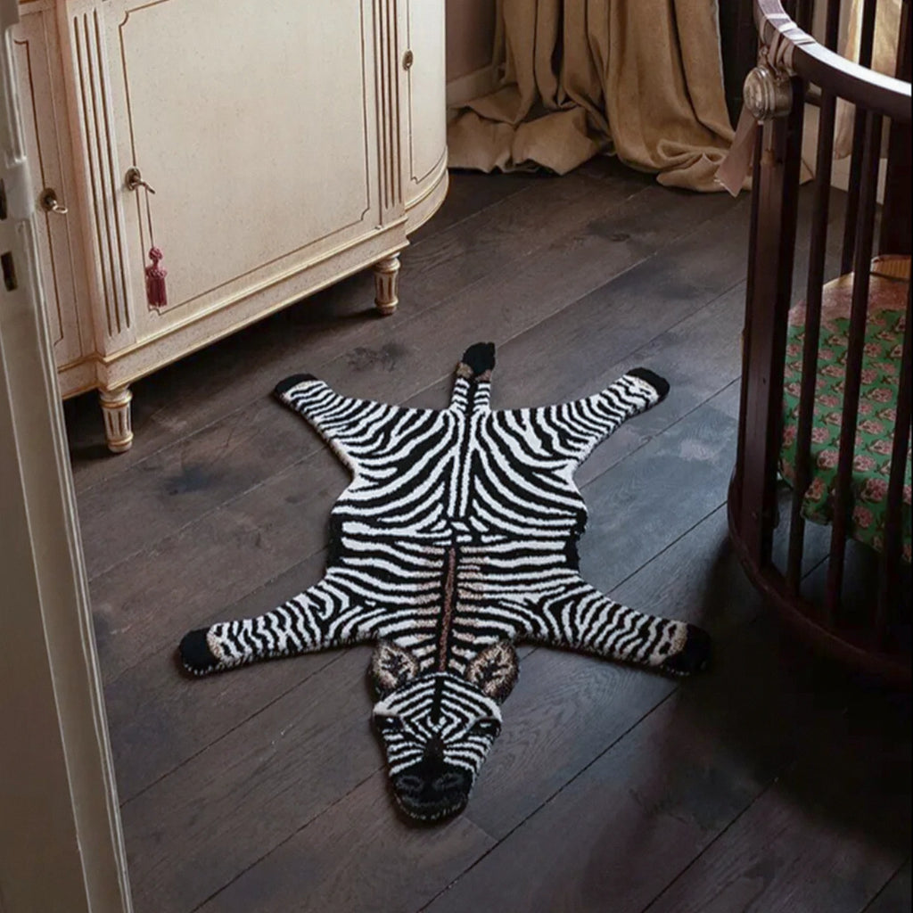Zibi small zebra animal shaped rug in black and white by Housenfriends on a wooden floor in a room with furniture.