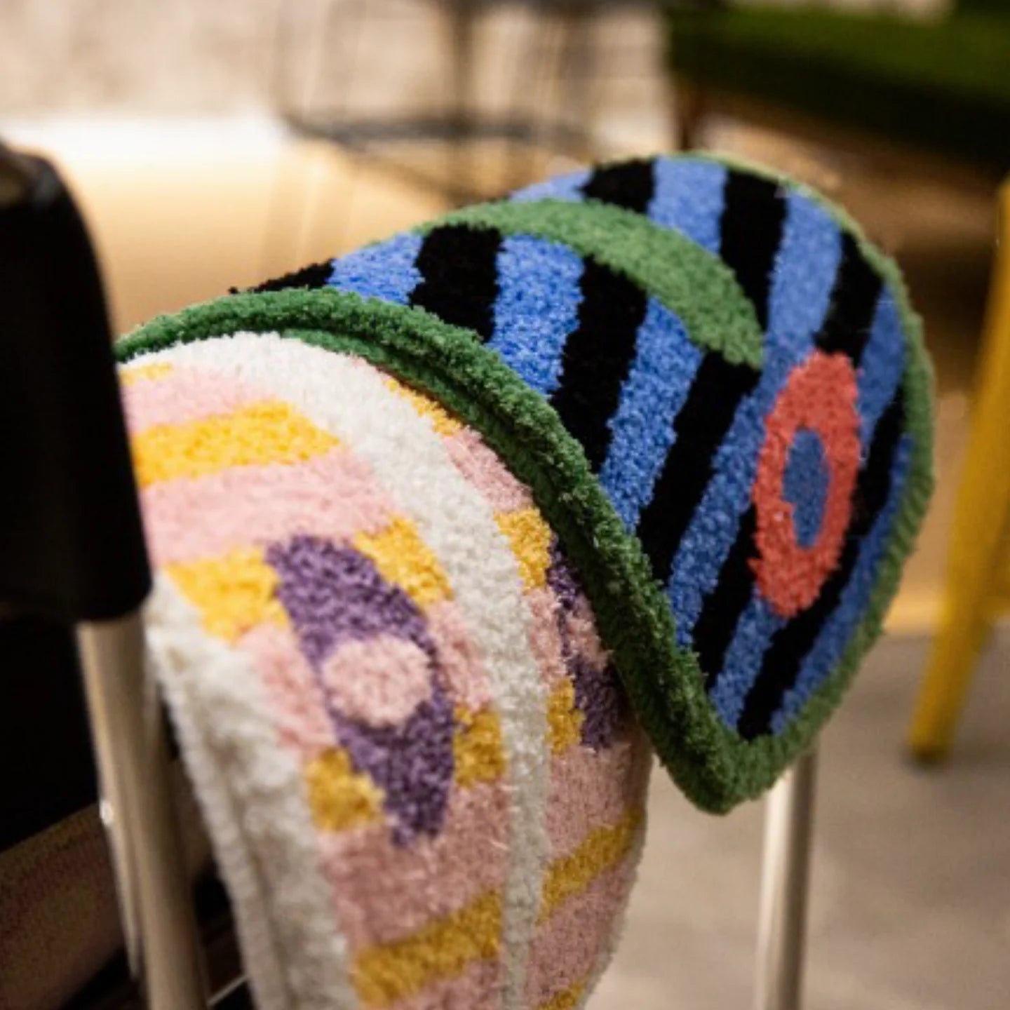 Milo pink and green small oval shaggy African mask rugs by Housenfriends draped over a wooden chair armrest