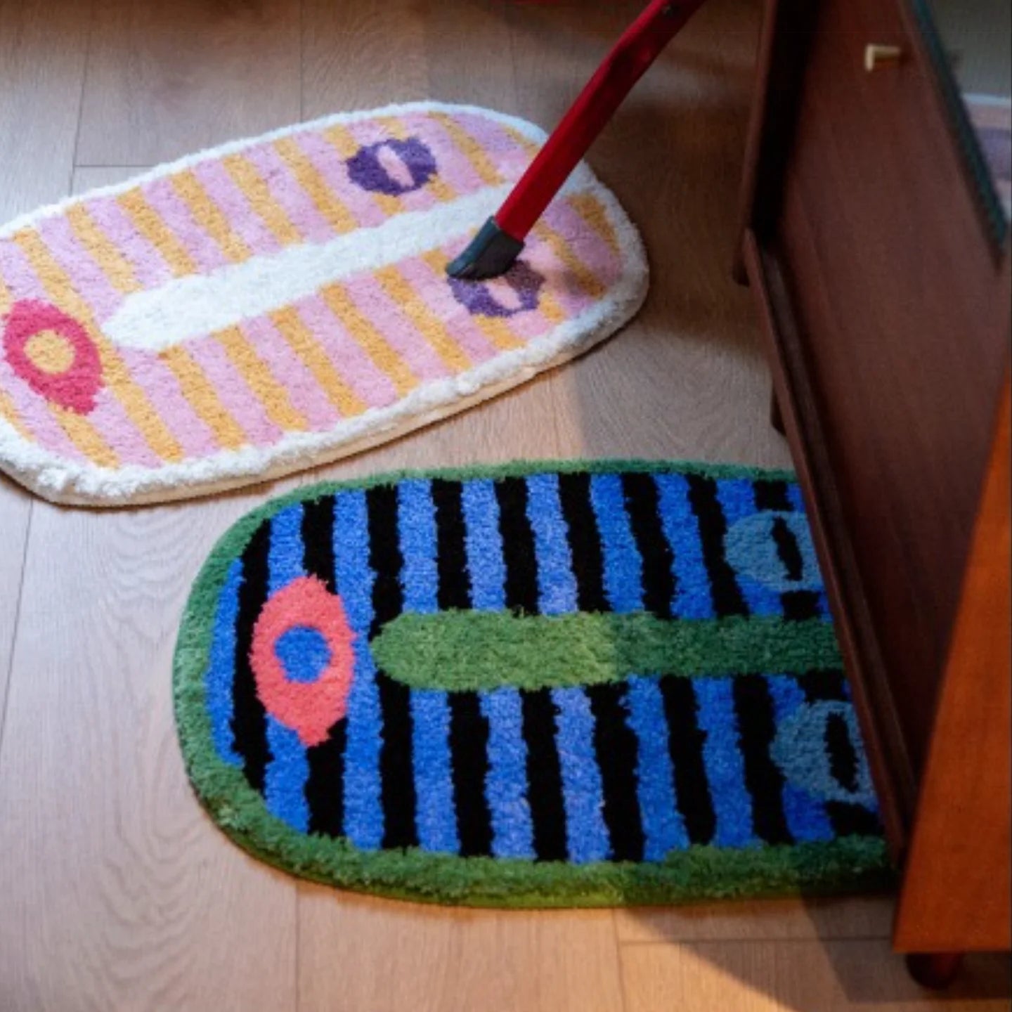 Milo pink and green small oval shaggy African mask rugs by Housenfriends on a wooden floor