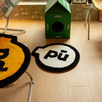 Pu yellow small shaggy graphic emblem rug with black outline by Housenfriends on a wooden floor next to a green box