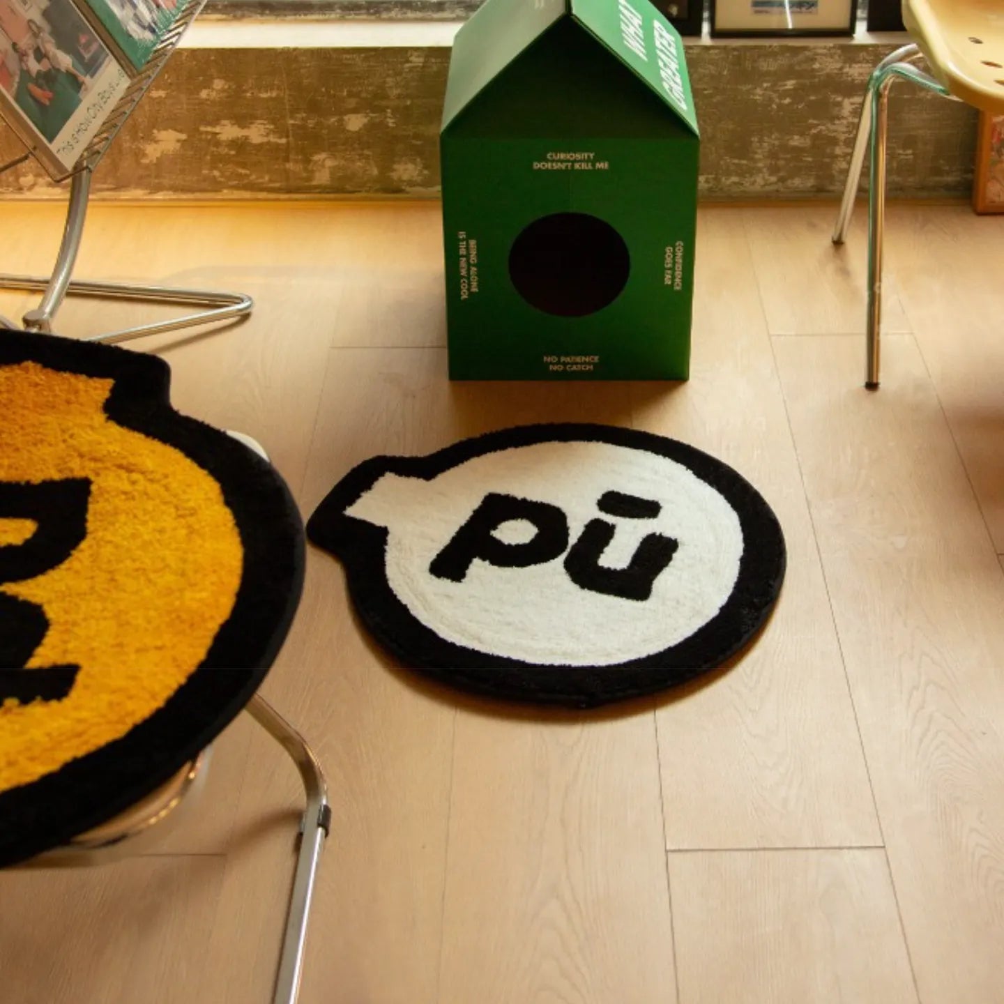 Pu yellow small shaggy graphic emblem rug with black outline by Housenfriends on a wooden floor next to a green box