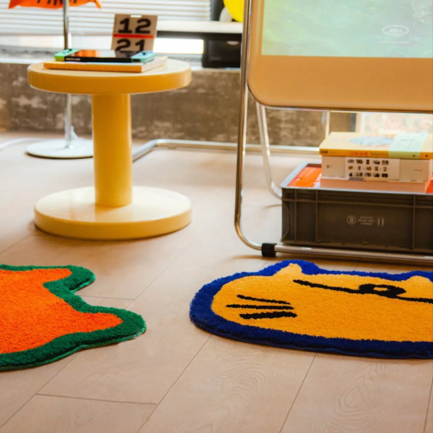 Doki orange bear-shaped rug and Poki yellow cat-shaped rug by Housenfriends on wooden floor with yellow stool and books