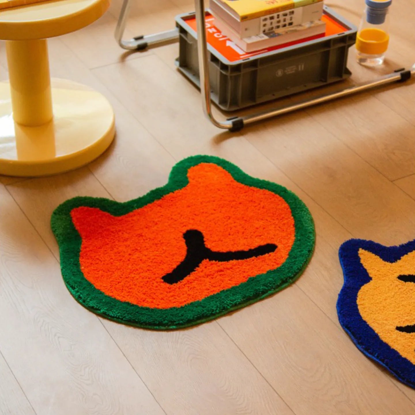 Doki orange small hand-tufted shaggy bear-shaped rug by Housenfriends on a wooden floor with a cart and stool