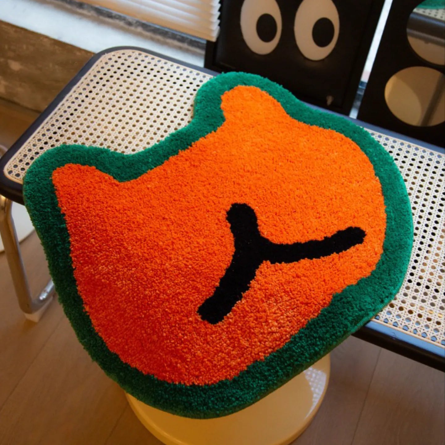 Doki orange small hand-tufted shaggy bear-shaped rug with green outline by Housenfriends on a woven table
