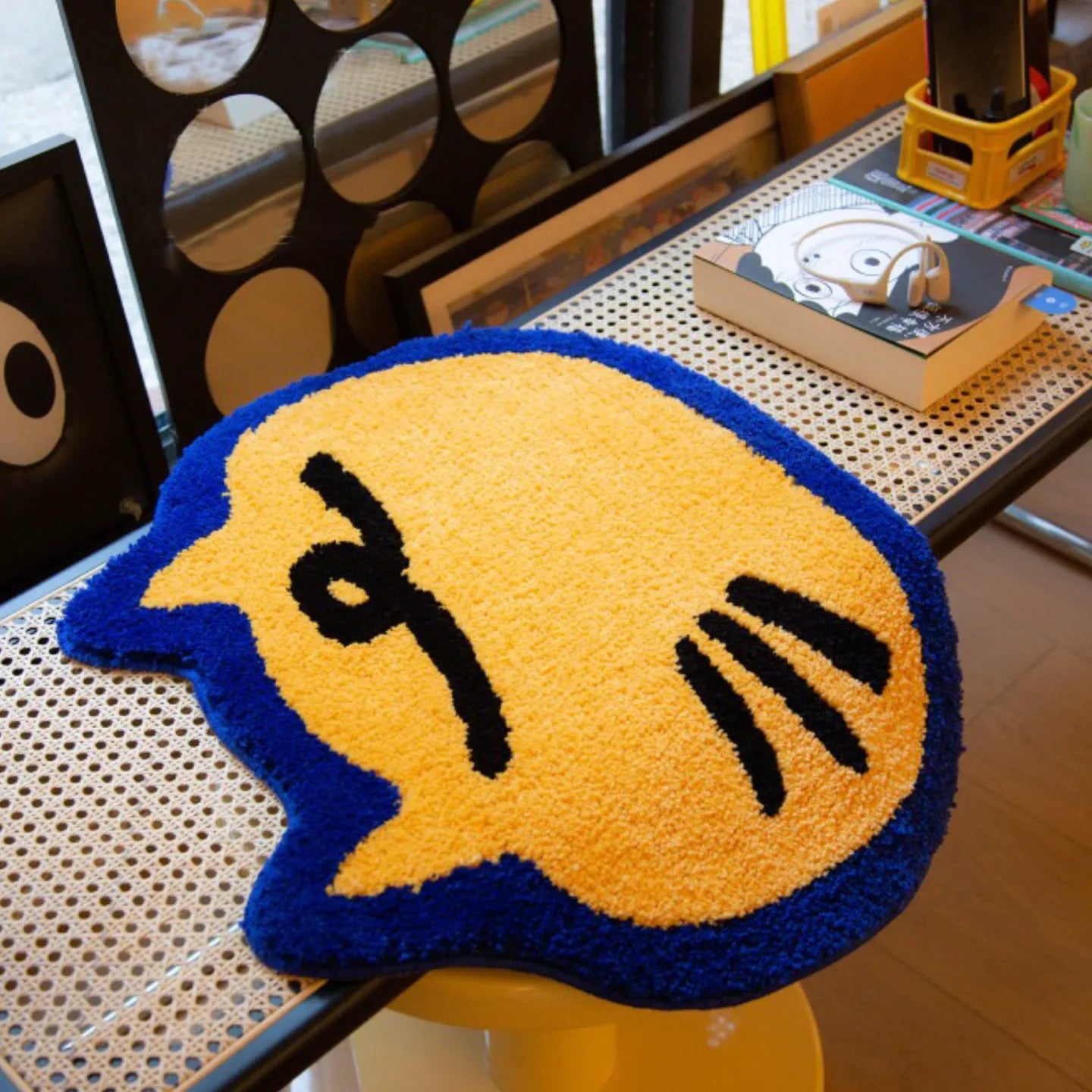 Poki yellow small shaggy cat-shaped rug with blue outline by Housenfriends on woven table with books