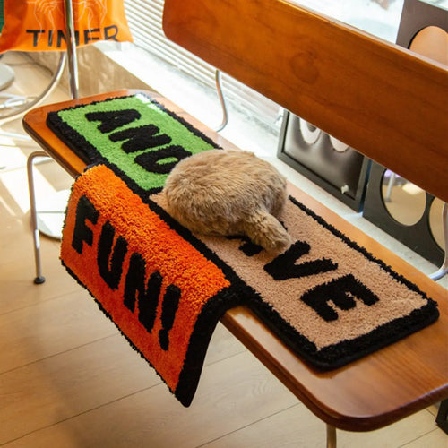 And Have Fun shaggy graphic word art rug in green, black, orange and beige by Housenfriends on a wooden surface