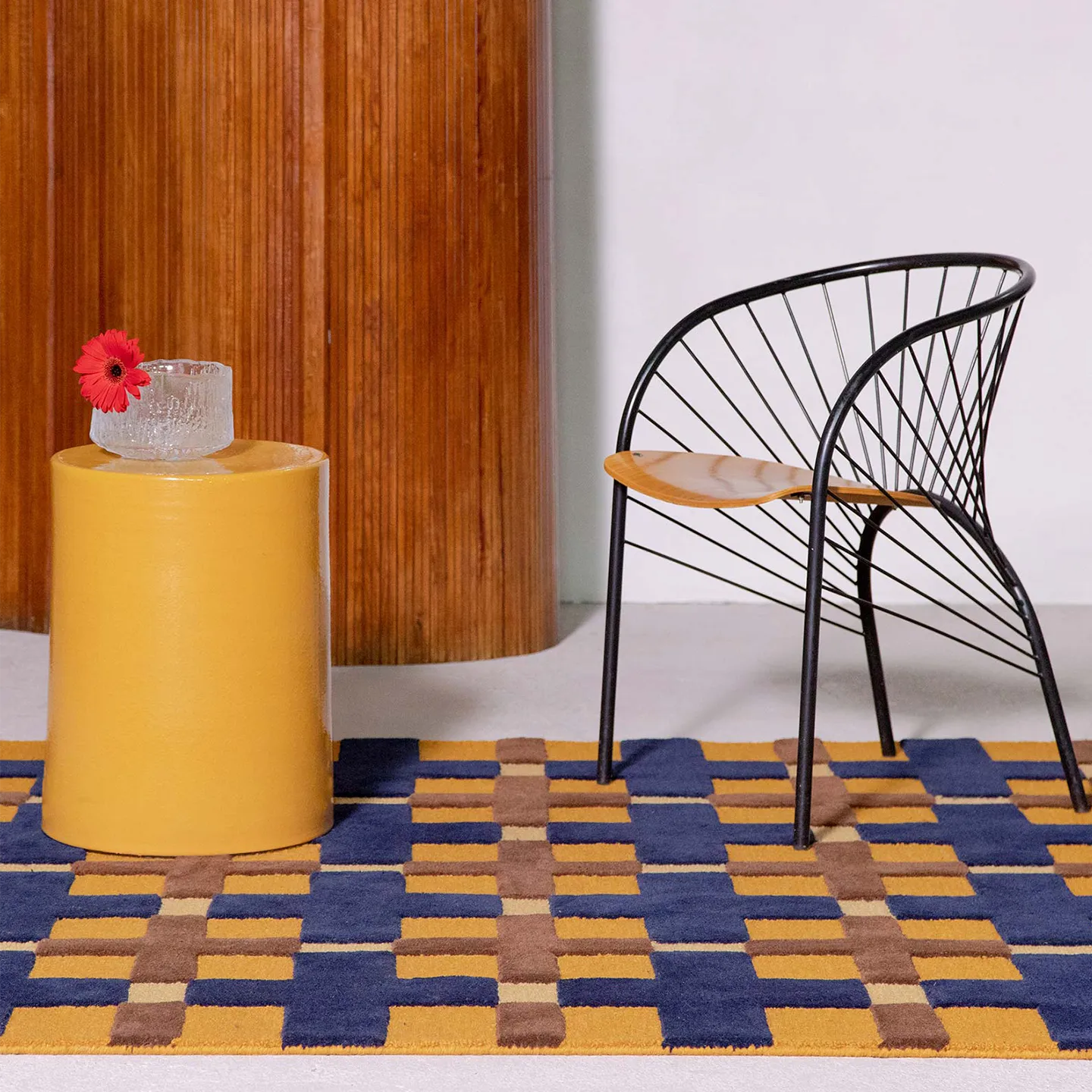 Yellow side table with a pink flower, black chair on Juno mustard, gold, and navy checkered tufted rug by Housenfriends