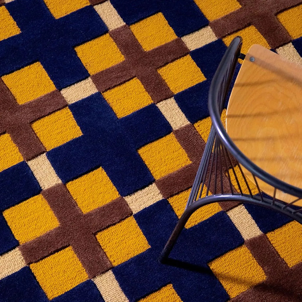 Close-up of the Juno mustard, gold, and navy checkered tufted rug by Housenfriends with a chair on top