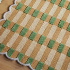 Close-up of pastel green and orange gingham wavy rug by Housenfriends on a wooden floor
