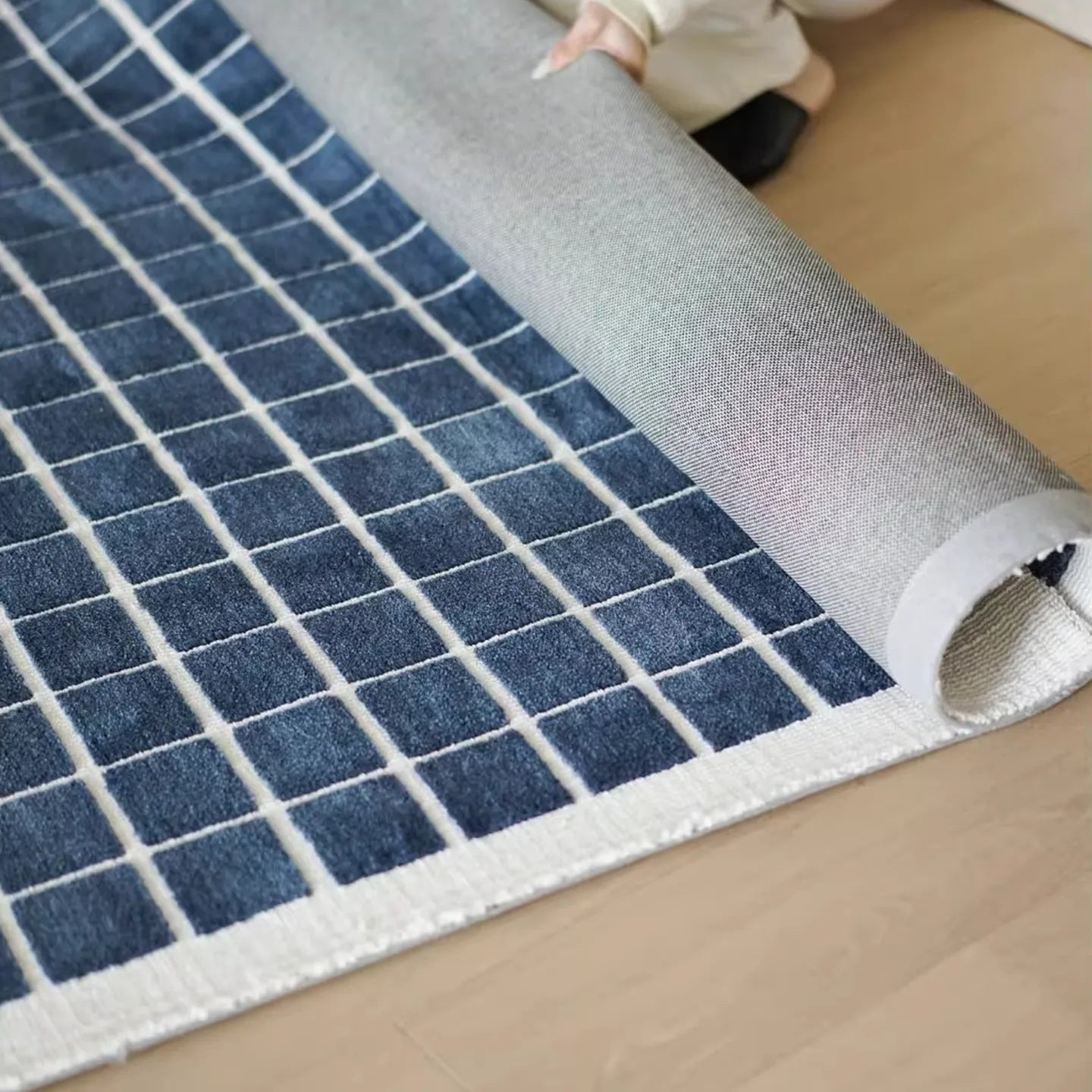 Roll of the Salina navy blue grid pattern modern rug by Housenfriends being unrolled on a wooden floor.