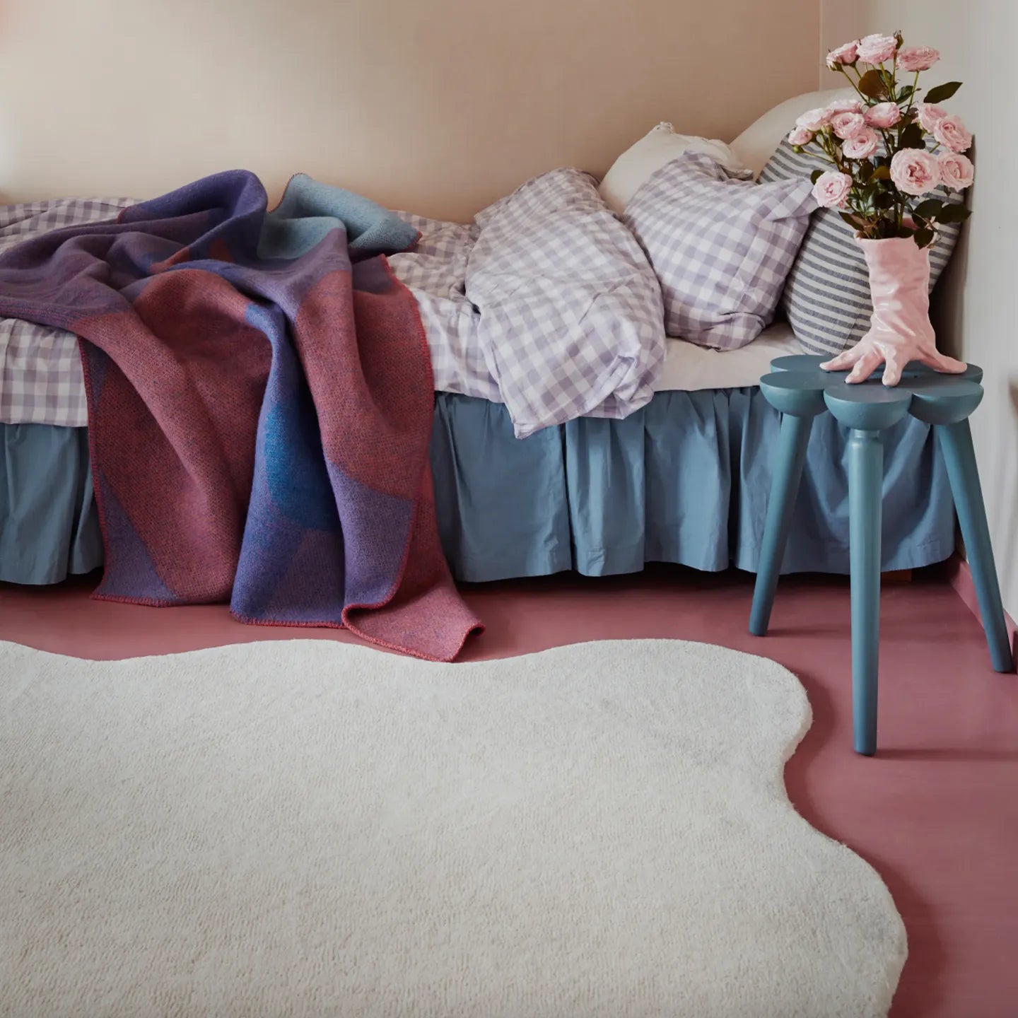Cora off-white irregular wavy rug by Housenfriends in a room with bed, blankets, pillows, and small table with flowers