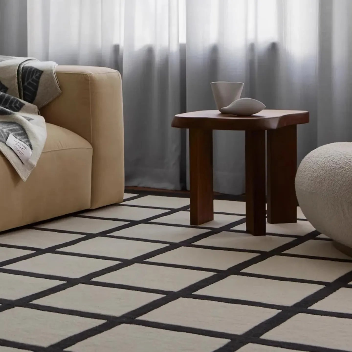 Living room with a beige sofa, wooden side table, and Studio Black and Cream Modern Grid Cut Pile Rug by Housenfriends