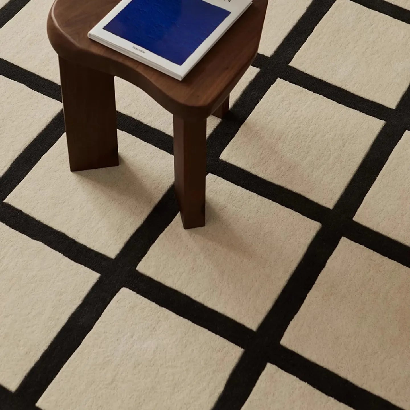 Wooden stool with a blue cushion on Studio Black and Cream Modern Grid Cut Pile Rug by Housenfriends