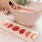 Eclipse pink and orange semi-circle shaggy runner rug by Housenfriends on bathroom floor with person reading in bathtub
