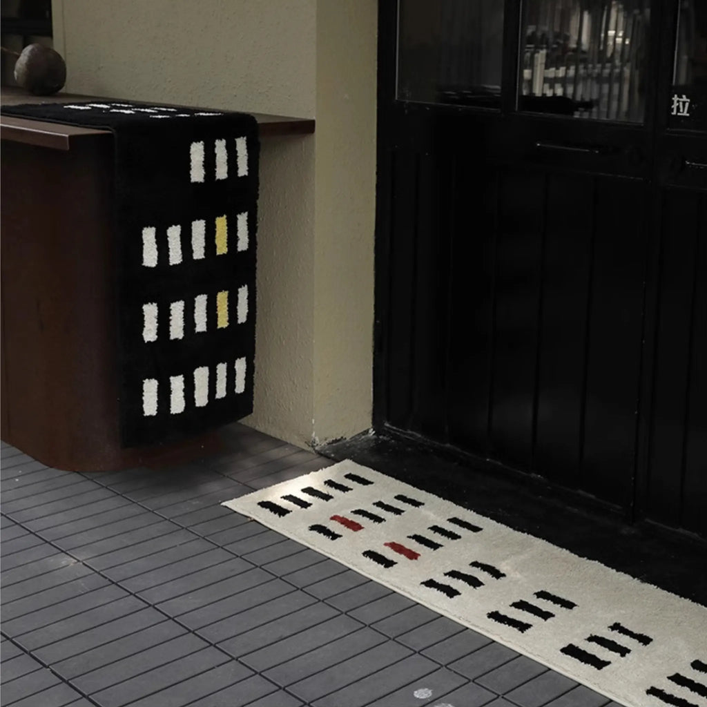 Arlo White and Black Asymmetric Checkered Tufted Runner by Housenfriends on a tiled floor next to a door.