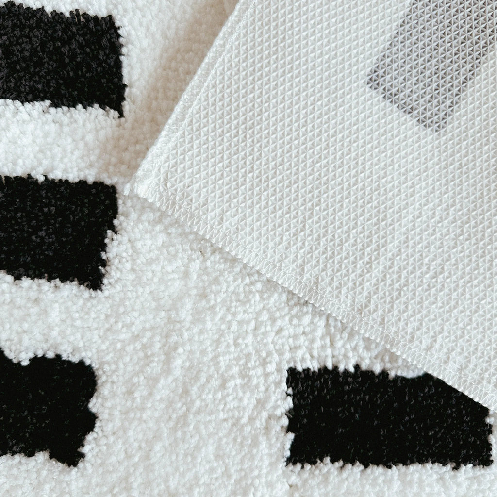 Close-up of a texture and a white non-slip backing of Arlo White and Black Asymmetric Checkered Tufted Runner Rug