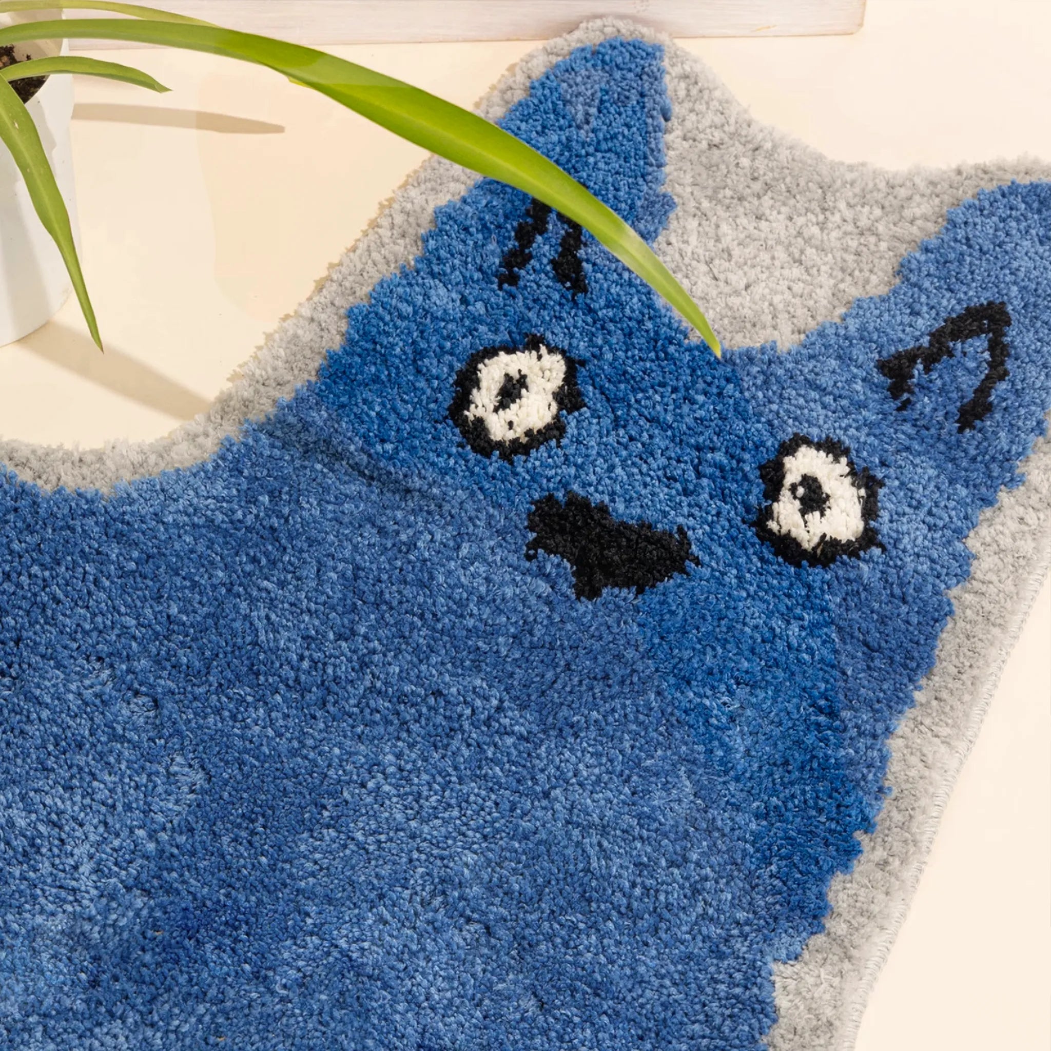 Close-up of Goofy Wide Eyed Blue Cat Shaped Tufted Rug on a light background